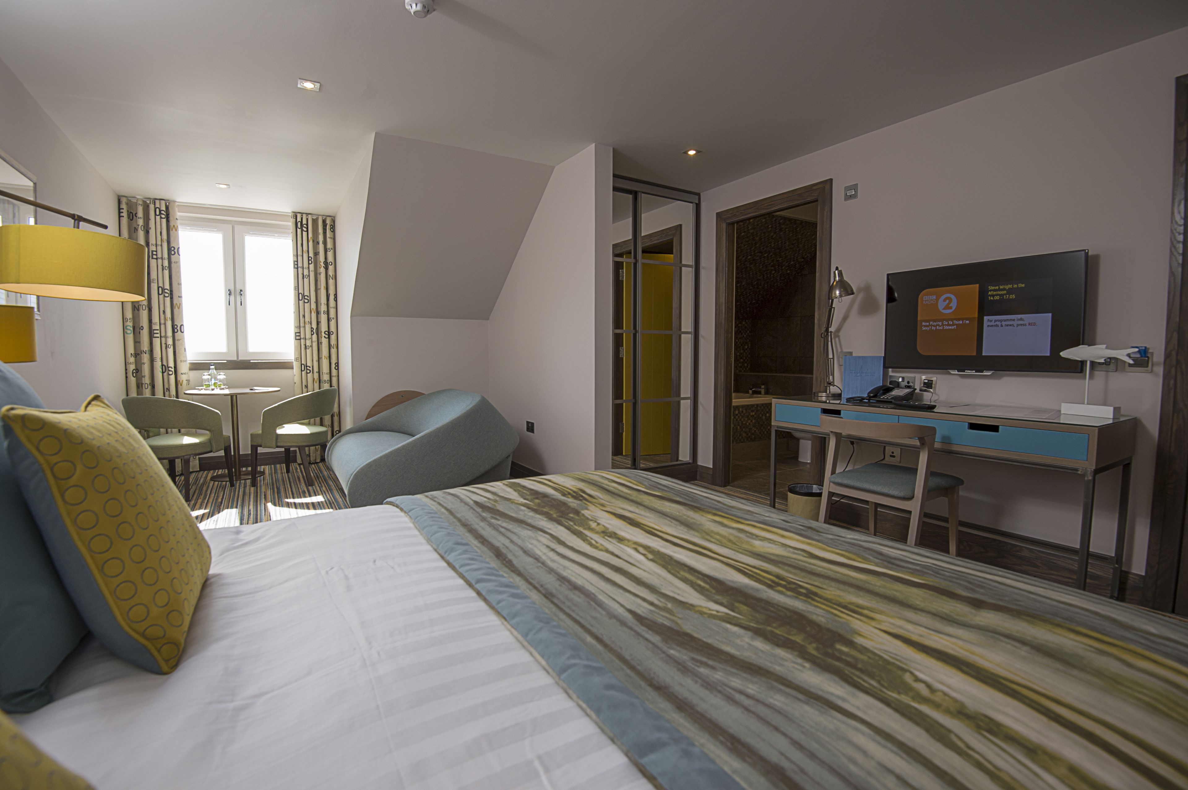 A hotel room with a bed, a desk, a chair, a TV, and a window.
