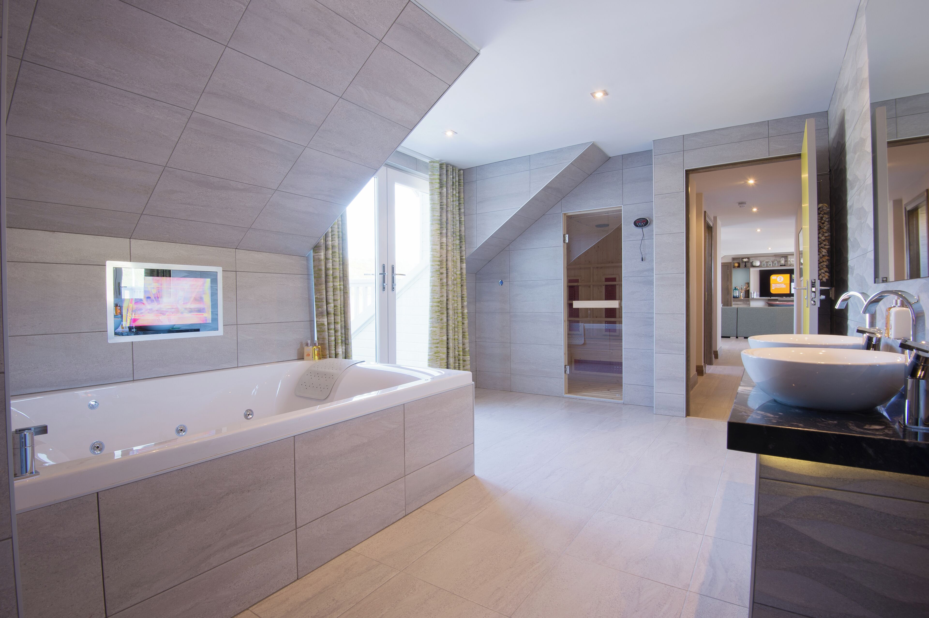 A modern bathroom with a large bathtub, a vanity with a large sink, and a television mounted on the wall.
