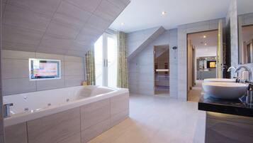A modern bathroom with a large bathtub, a vanity with a large sink, and a television mounted on the wall.