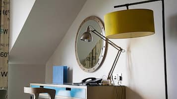 Un bureau avec une lampe, un miroir et une boîte bleue sur un mur blanc.