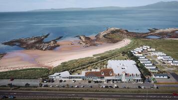 Vista aérea de una zona costera con playa, aparcamiento y una hilera de viviendas móviles.