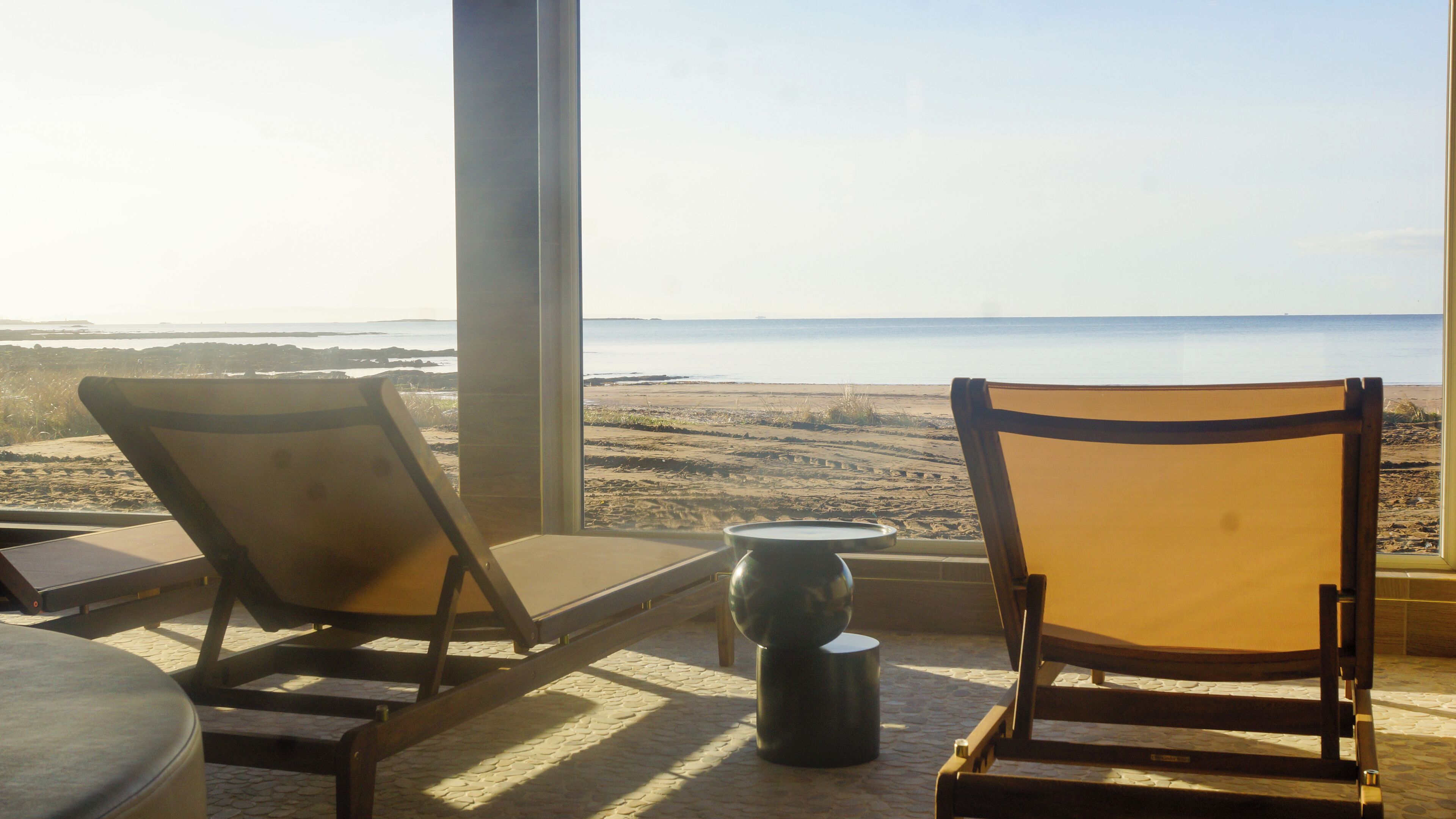 Two wooden lounge chairs facing a beach view through large windows.