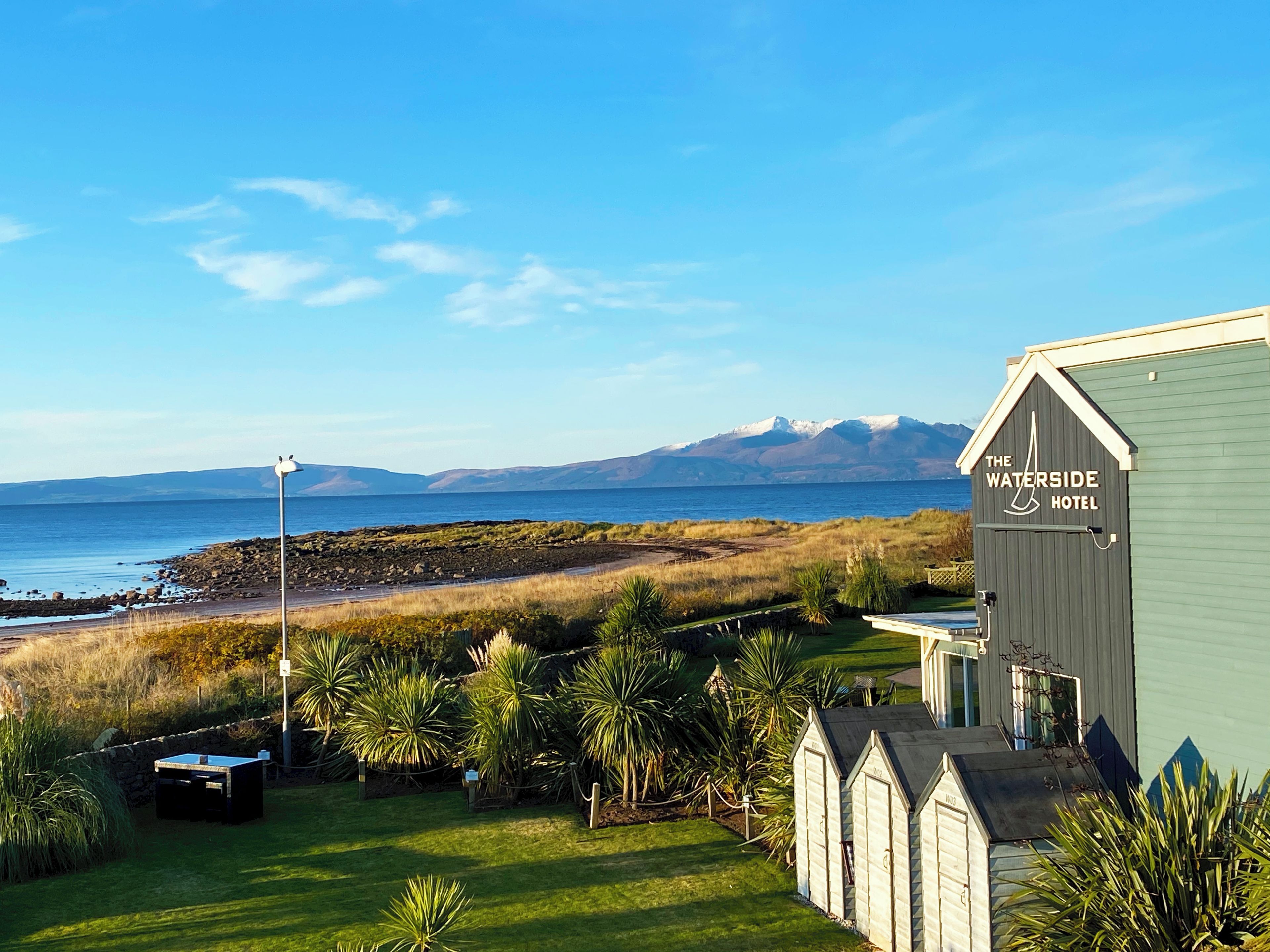 A hotel with a view of the sea and mountains, featuring a well-maintained lawn and a signboard.