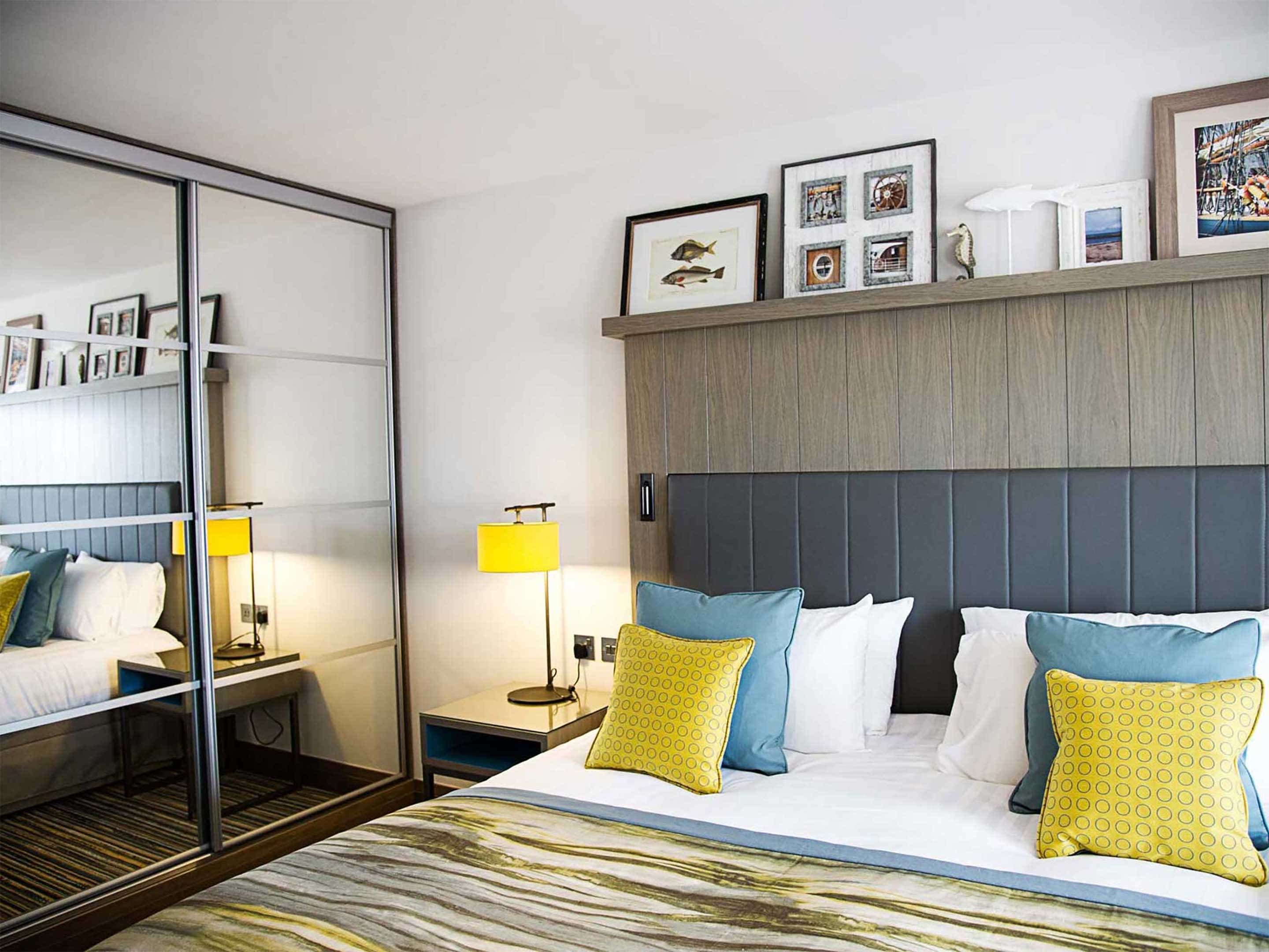 A hotel room with a bed, bedside tables, a mirror, and a wall with framed pictures.