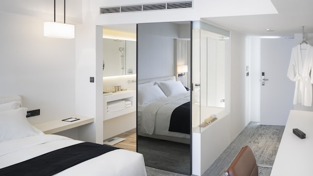 Habitación de hotel moderna con cama, zona de estar, baño con ducha y vestidor.
