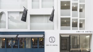 Fachada del HOTEL SWIIO con amplias ventanas, un toldo azul y dos banderas negras.