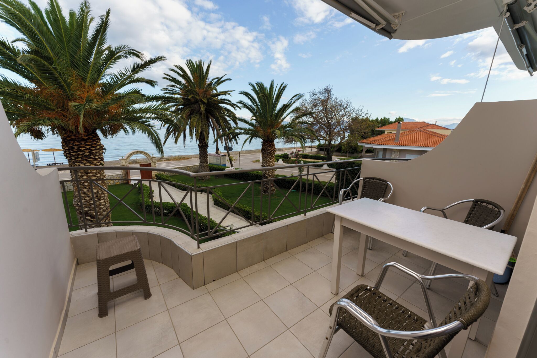 A balcony with a table and chairs, overlooking a garden with palm trees and a view of the sea.