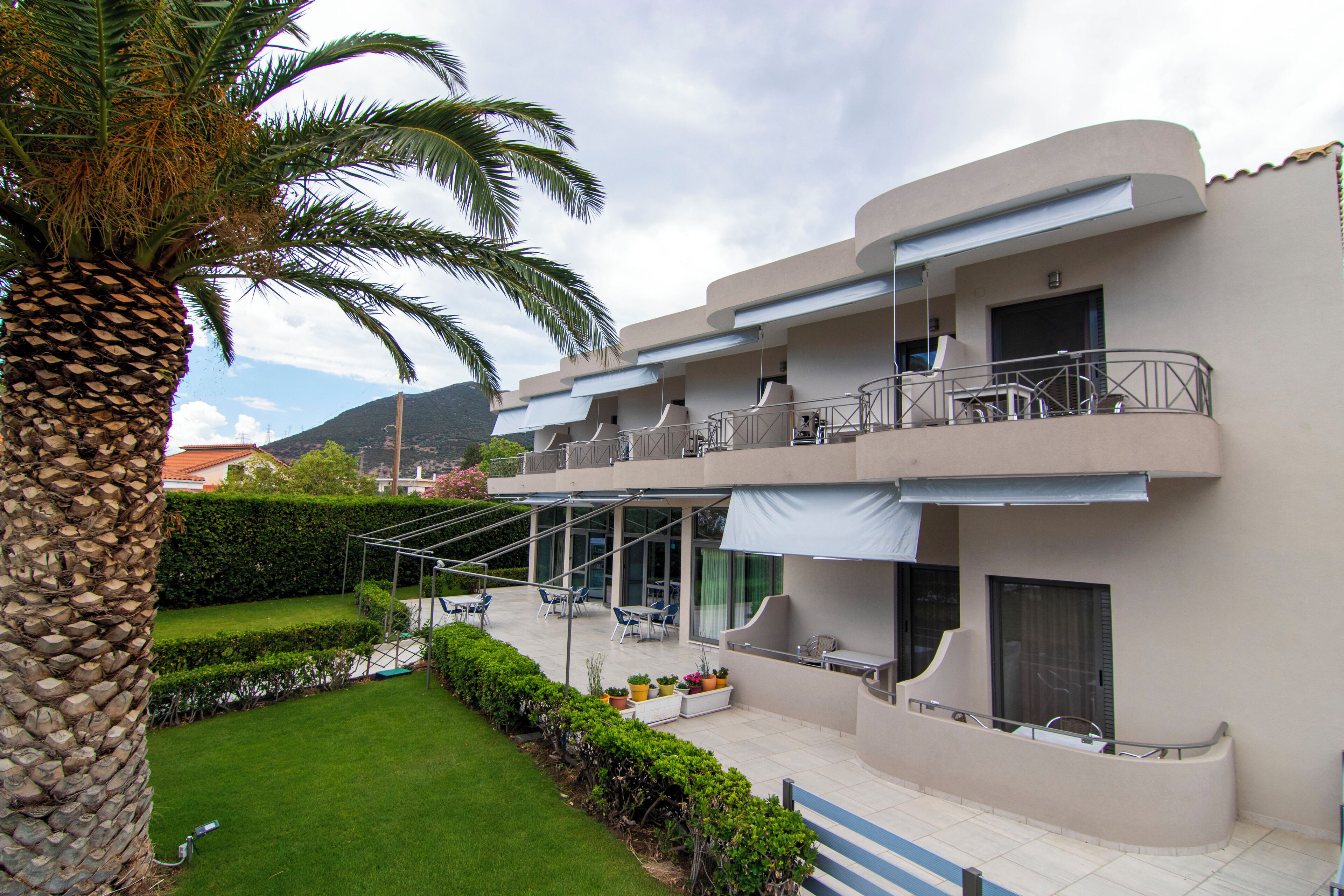 A modern two-story building with a balcony, outdoor seating area, and a well-maintained garden.