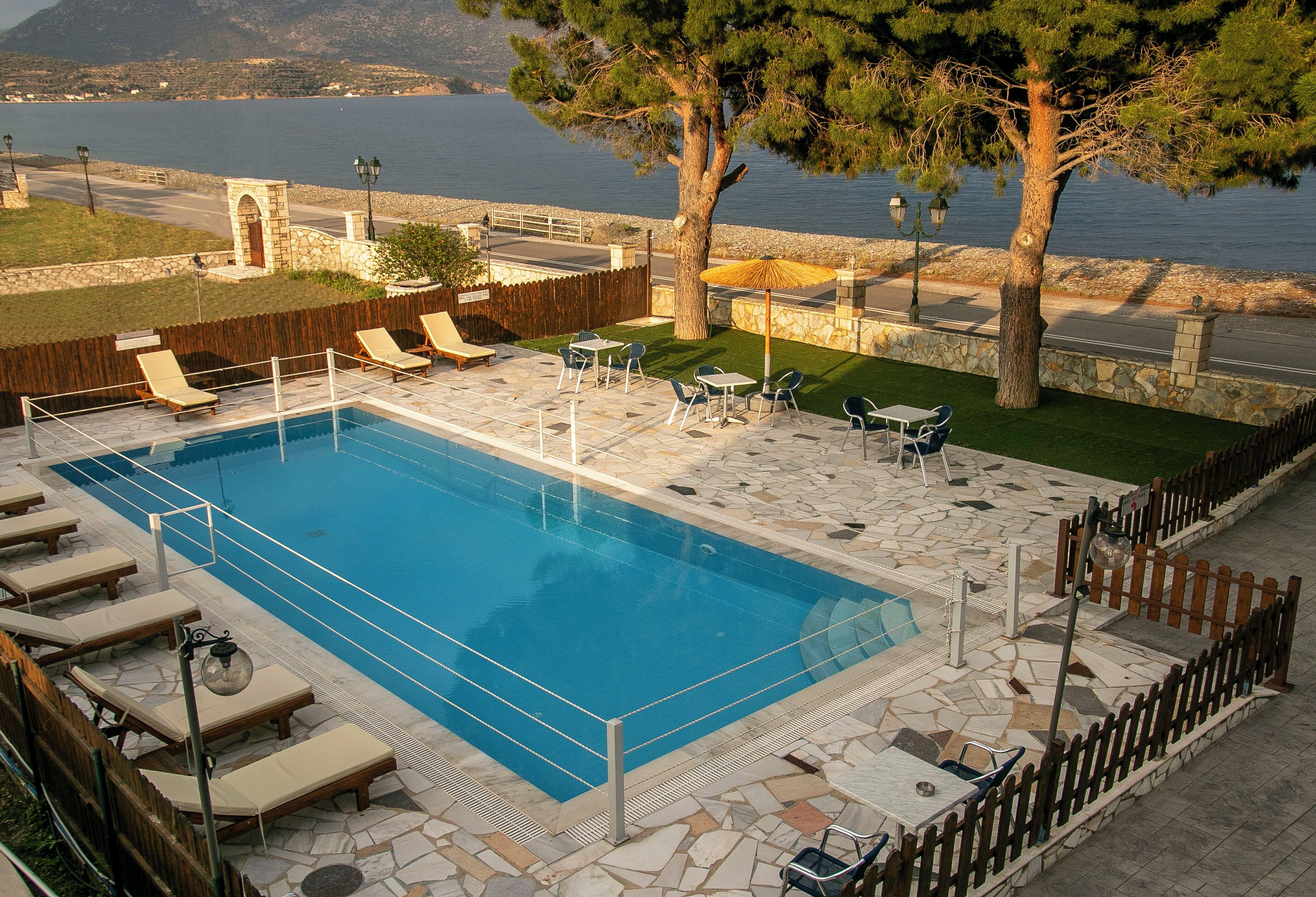 A swimming pool with lounge chairs and tables, surrounded by stone tiles and a wooden fence.