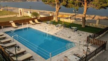 A swimming pool with lounge chairs and tables, surrounded by stone tiles and a wooden fence.