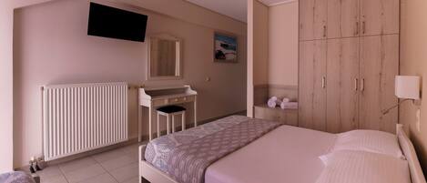 A bedroom with a bed, a desk, a wardrobe, a radiator, and a TV mounted on the wall.