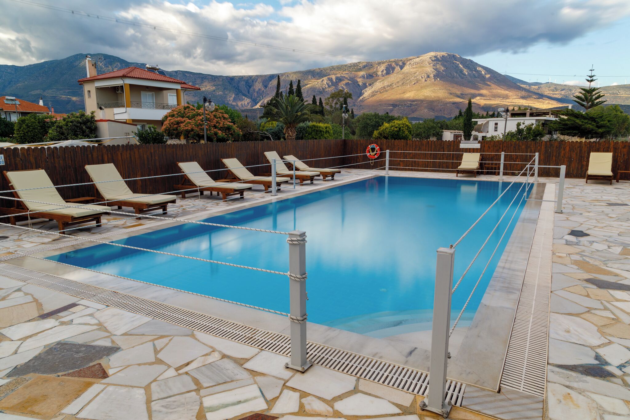 Una piscina con sillones de descanso, una valla de madera y montañas al fondo.
