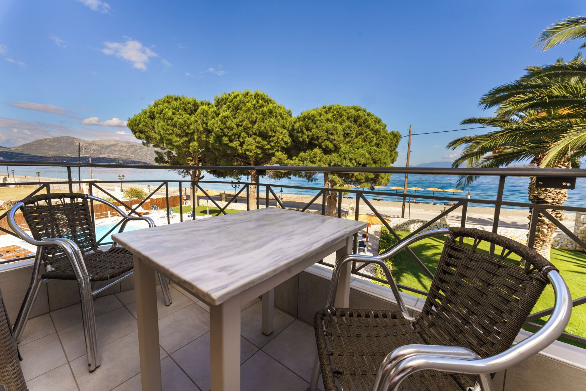 Un balcon avec une table et des chaises, donnant sur une piscine et une plage.