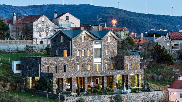 A stone building with multiple windows and balconies, surrounded by greenery and a hillside. - A Casa do Tio Tenente (Serta)