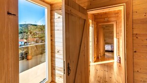 A wooden interior with a large window, a door leading to another room, and a visible bed. - A Casa do Tio Tenente (Serta)