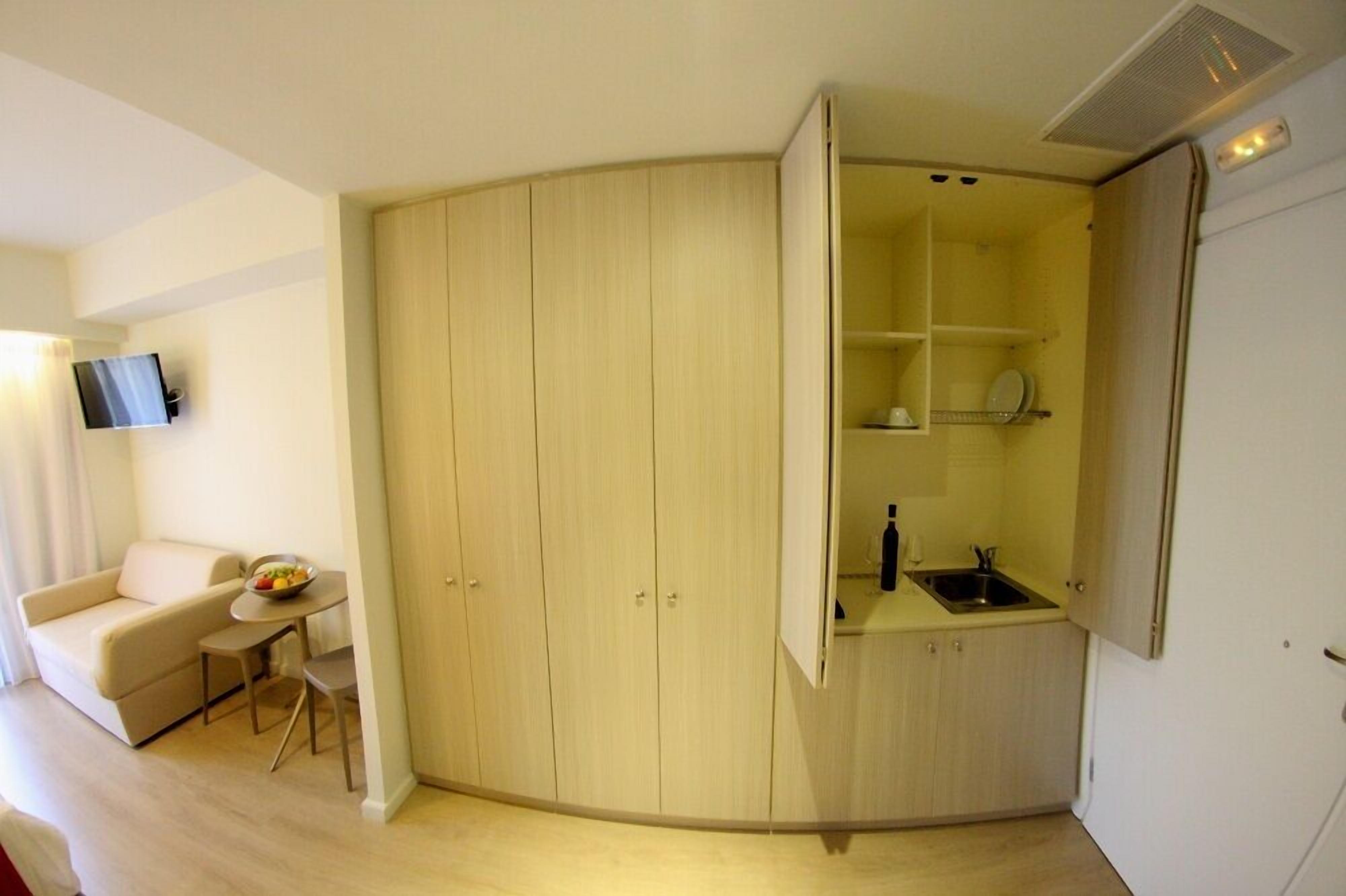 A compact room with a kitchenette, a dining area, and a TV mounted on the wall.