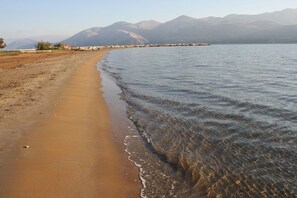 Una playa con agua cristalina, una orilla arenosa y montañas al fondo.