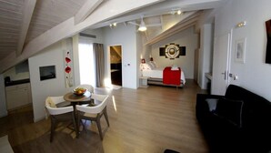 A modern apartment with a dining area, a living room with a black sofa, a kitchen, and a bedroom with a red accent wall. - Aura Boutique Hotel (Kefalonia)