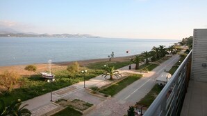 A coastal view with a beach, a road, and a building with a balcony overlooking the sea. - Aura Boutique Hotel (Kefalonia)