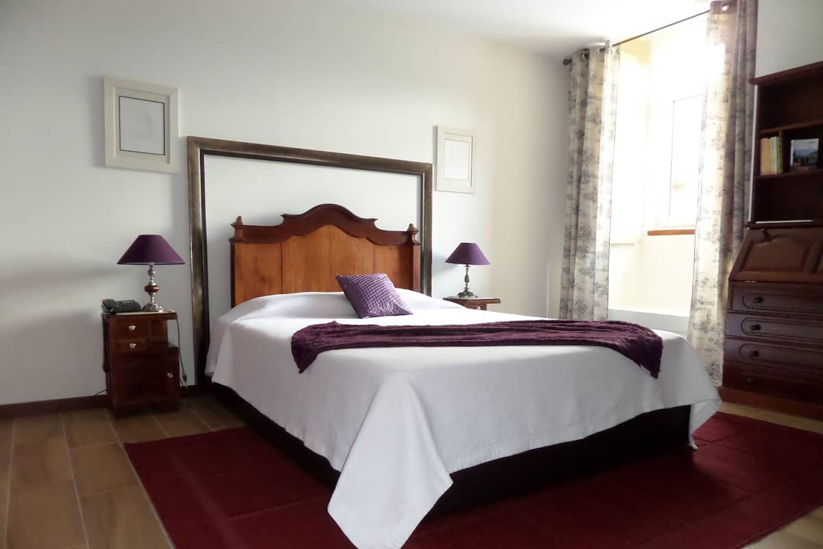 A neatly made bed with a wooden headboard, two bedside tables with lamps, a red rug, and a dresser with a mirror.