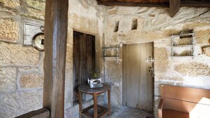 A rustic room with stone walls, a wooden bench, a sewing machine on a small table, and a metal shelf with glasses. - Casa Grande do Seixo (Chaves)