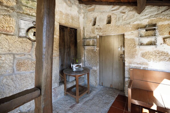 A rustic room with stone walls, a wooden bench, a sewing machine on a small table, and a metal shelf with glasses. - Casa Grande do Seixo (Chaves)
