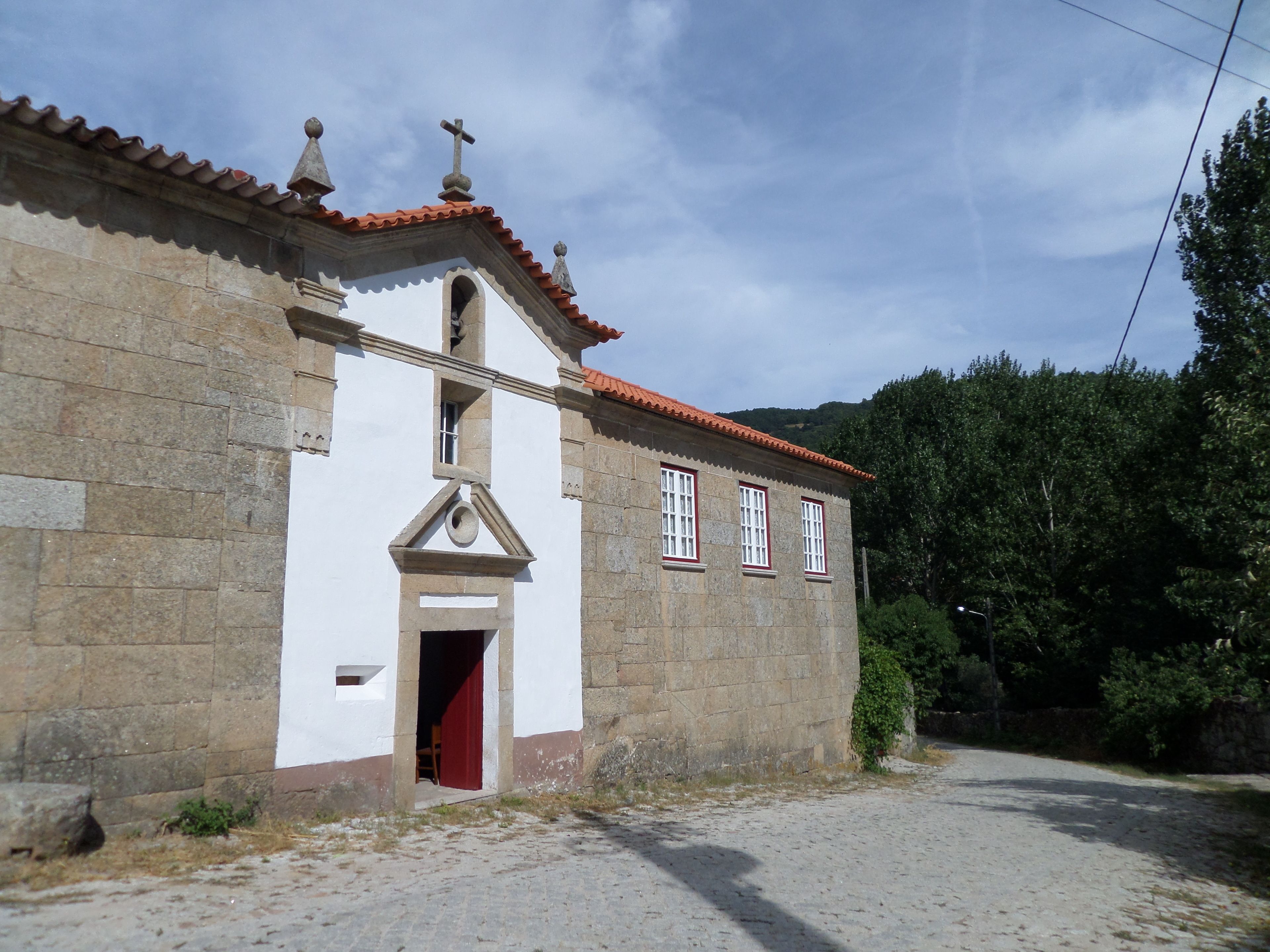 A stone building with a red-tiled roof, a bell tower, and a doorway.