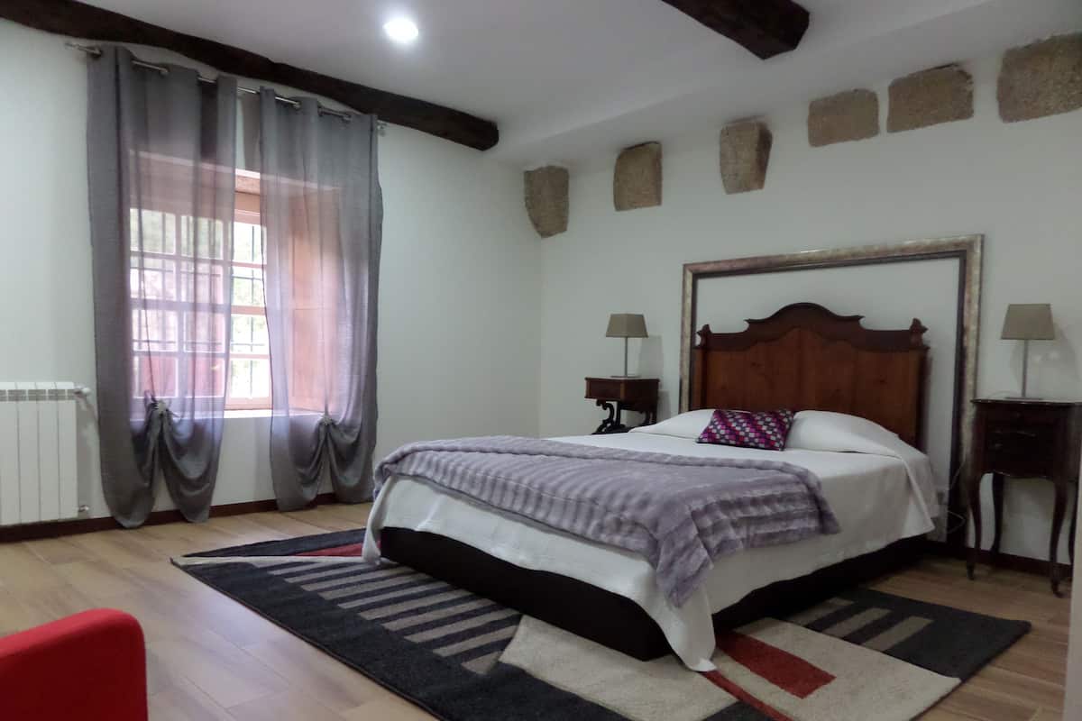 A bedroom with a wooden bed, a nightstand, a lamp, a window with curtains, and a radiator.