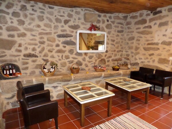 A stone-walled room with two wooden tables, chairs, and baskets containing wine bottles and fruits.