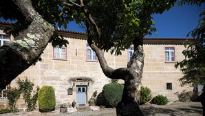 A stone building with a tiled roof, a central entrance with a blue door, and a paved courtyard. - Casa Grande do Seixo (Chaves)