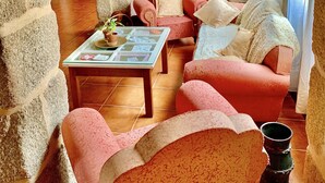 A cozy living room with stone walls, a wooden ceiling, and a mix of red and beige furniture. - Casa Grande do Seixo (Chaves)