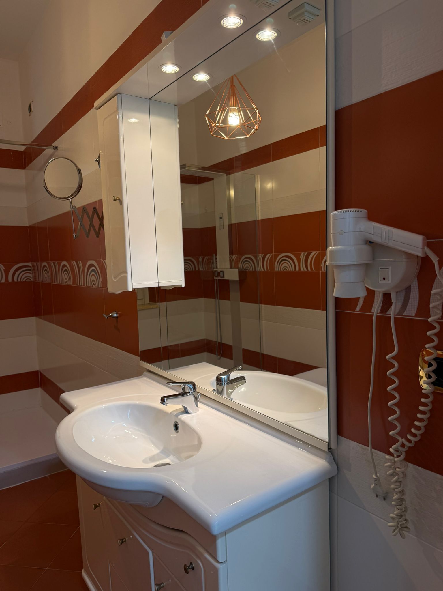 A bathroom with a white sink, a mirror, a hairdryer, and a shower.