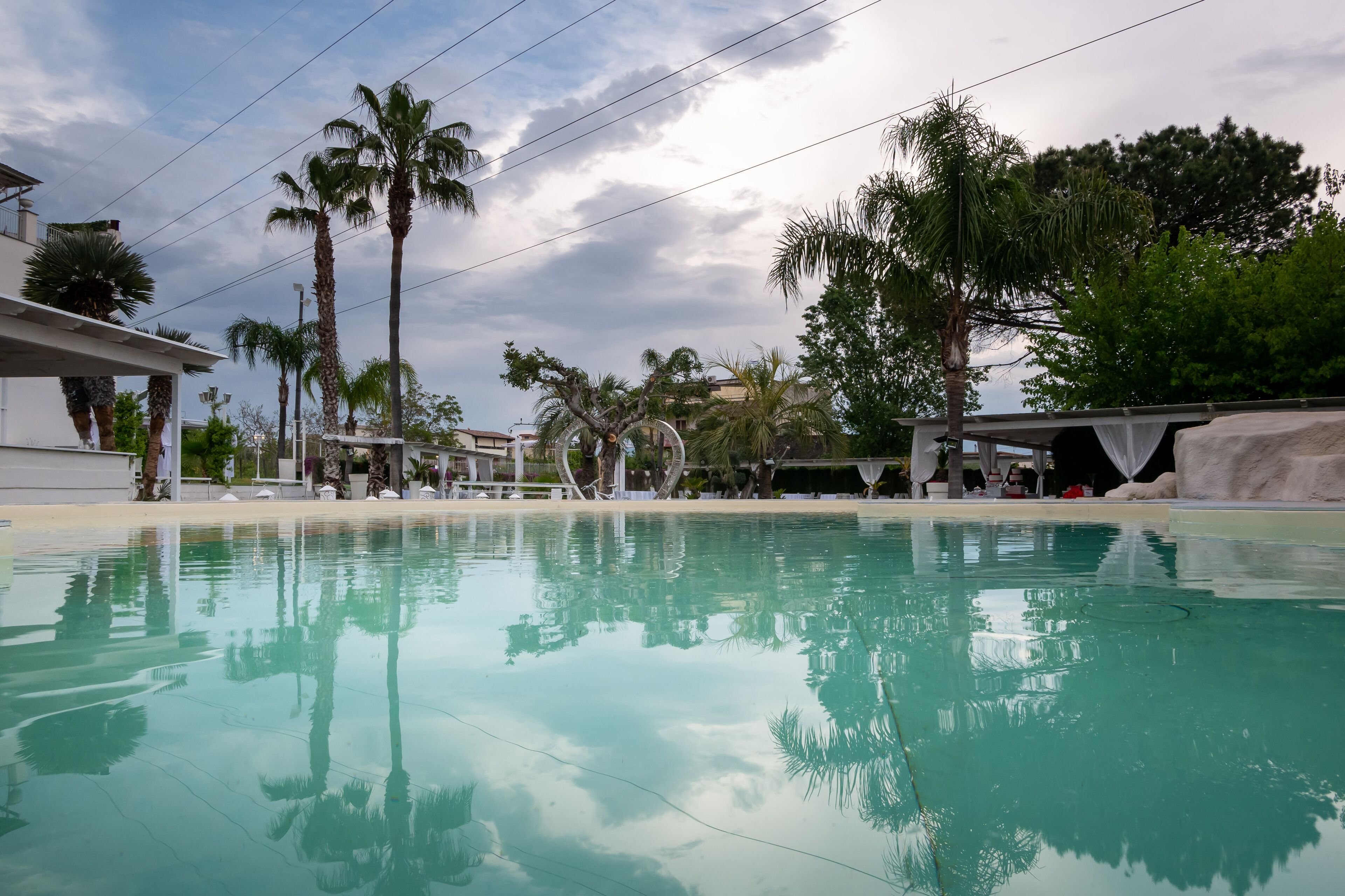 Ein Swimmingpool mit klarem Wasser, das Palmen und ein Gebäude im Hintergrund spiegelt.