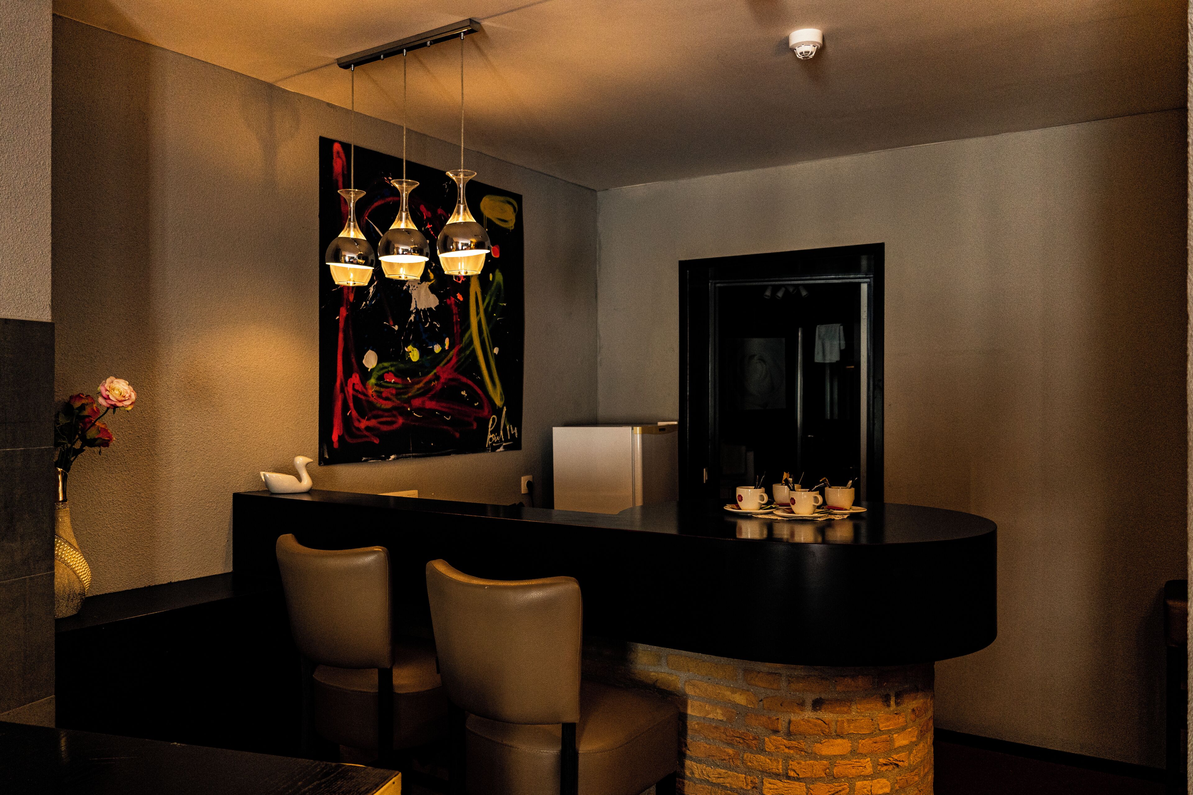 A modern bar area with a stone column, two chairs, a large abstract painting, and pendant lighting.
