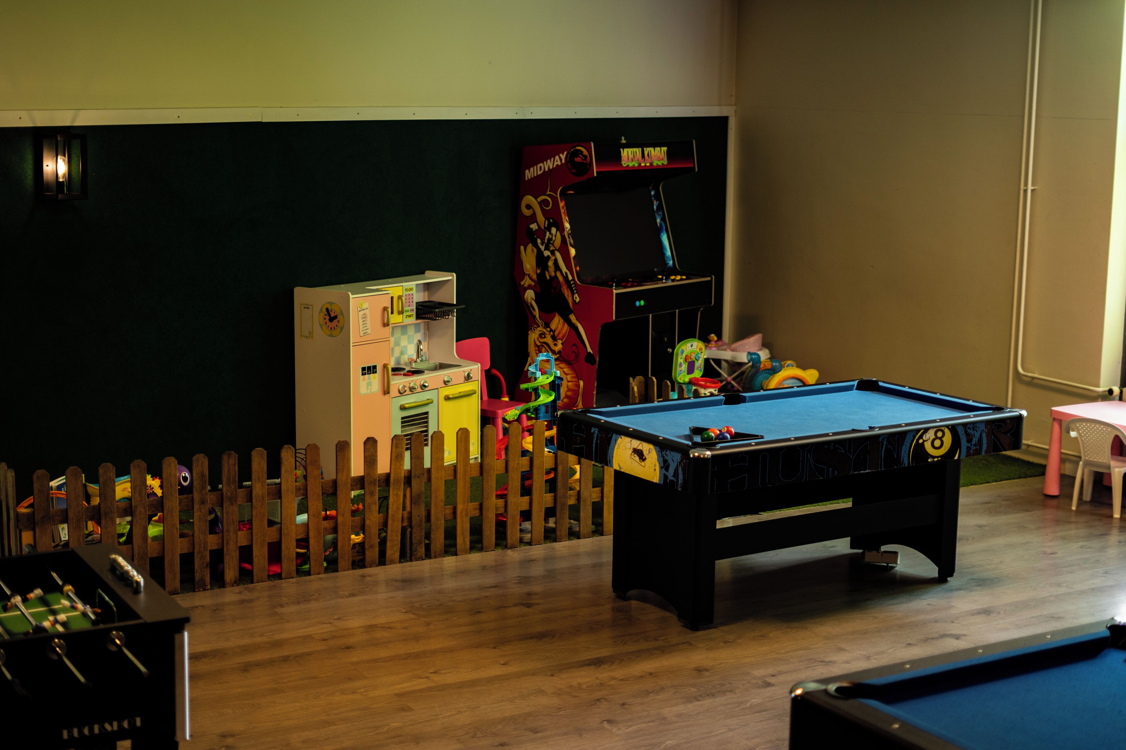 Een pooltafel, een tafelvoetbalspel en een flipperskast in een ruimte met een houten hek.