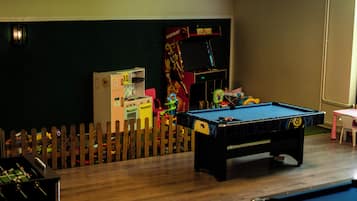 Een pooltafel, een tafelvoetbalspel en een flipperskast in een ruimte met een houten hek.