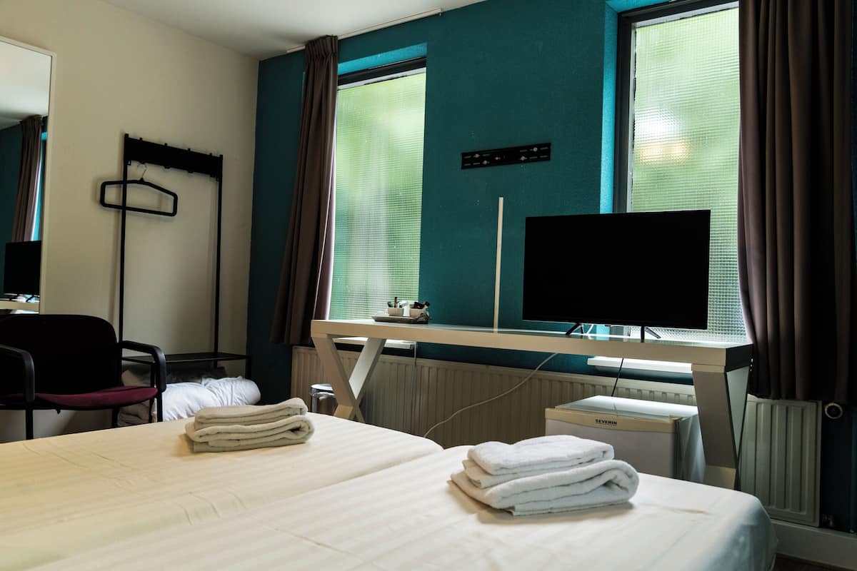 Una habitación de hotel con una cama, un escritorio con una computadora, una silla y un televisor.
