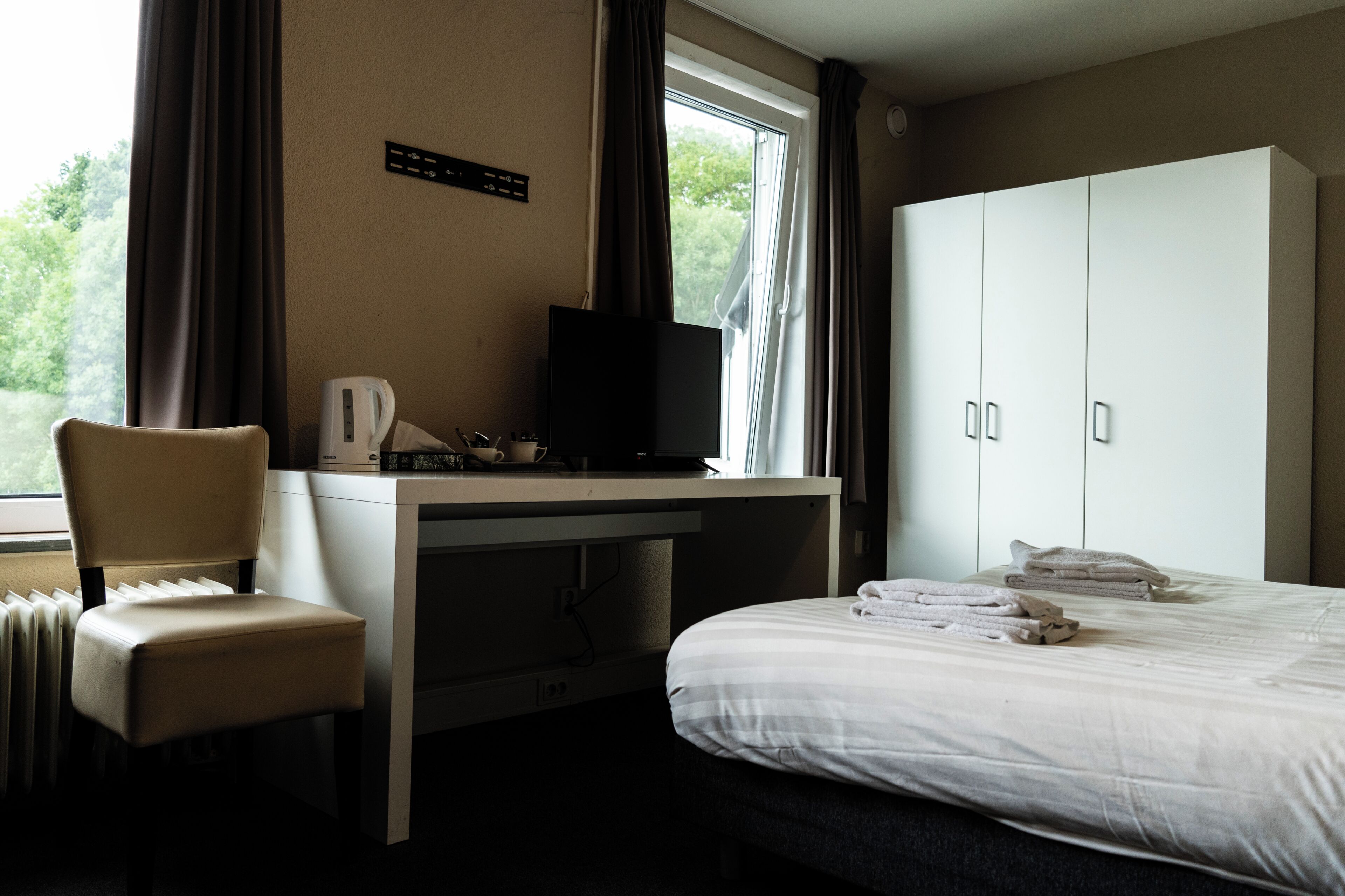 Een hotelkamer met een bed, een bureau met een televisie, een stoel en een kledingkast.