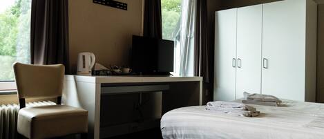 Una habitación de hotel con cama, escritorio con televisor, silla y armario.