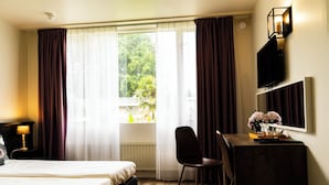 A hotel room with a bed, a desk, a chair, a TV, and a window with curtains. - Hotel de Elderschans (Aardenburg)