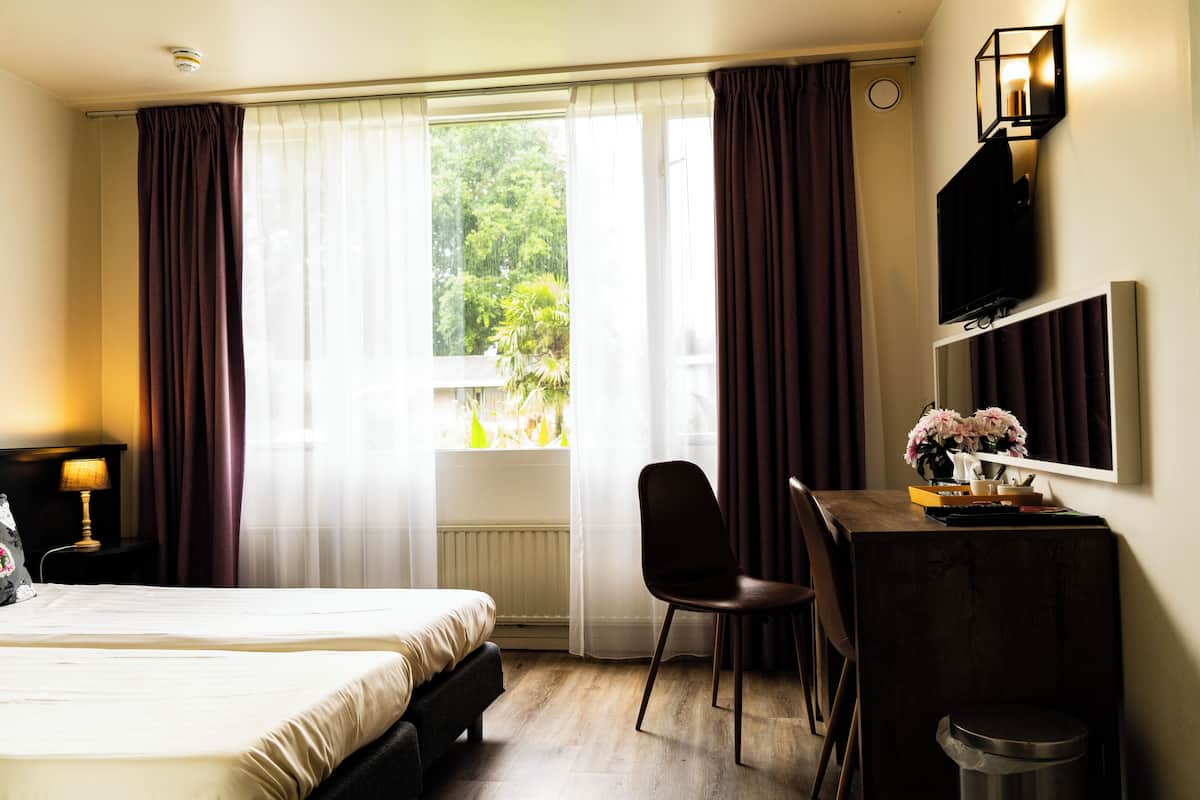 Habitación de hotel con cama, escritorio, silla, televisión y ventana con cortinas.
