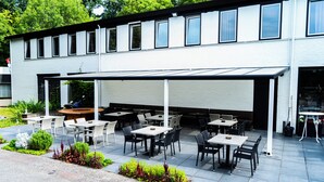 An outdoor patio area with tables and chairs, a covered seating area, and a building with multiple windows. - Hotel de Elderschans (Aardenburg)