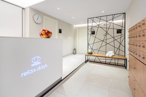 Ein Empfangsbereich mit einem 'Relax Days'-Schild, einer Uhr, einer Obstschale, einer Bank mit Handtüchern und Schließfächern.