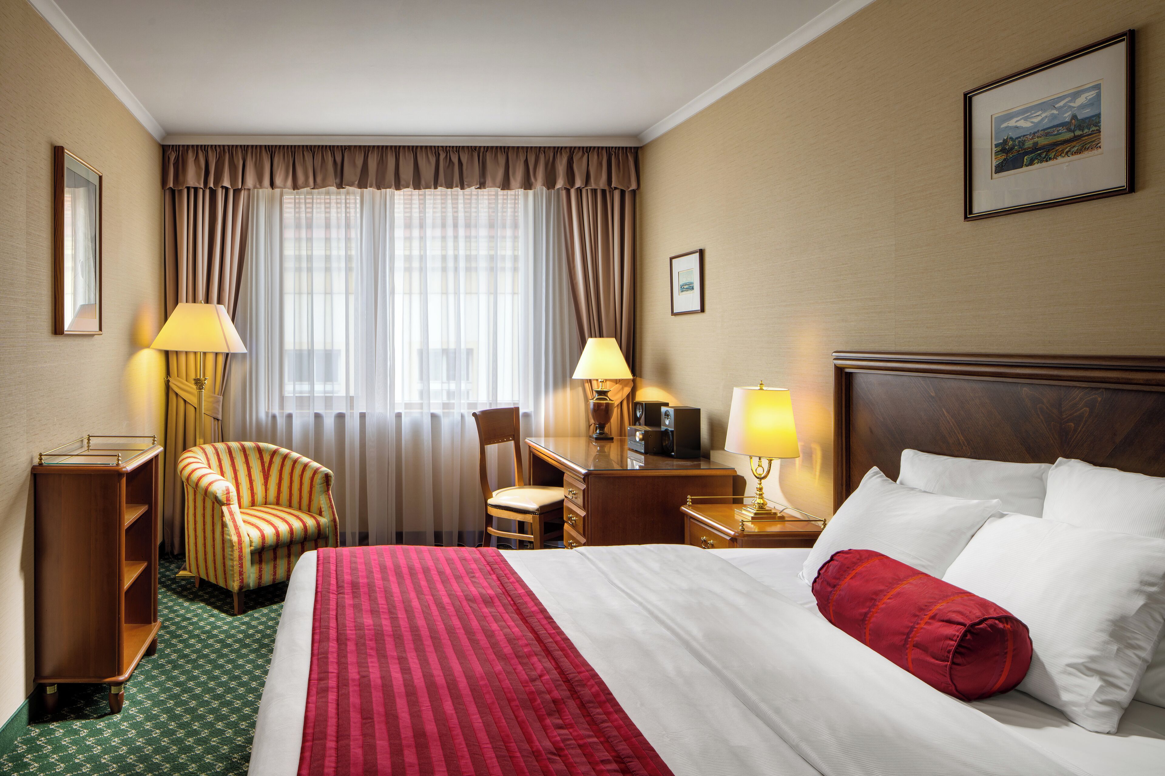 Ein Hotelzimmer mit einem Bett, zwei Stühlen, einem Schreibtisch, einer Lampe und einem Bild an der Wand.