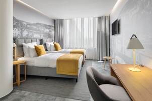 Quarto de hotel moderno com duas camas, uma escrivaninha, uma cadeira e uma televisão.