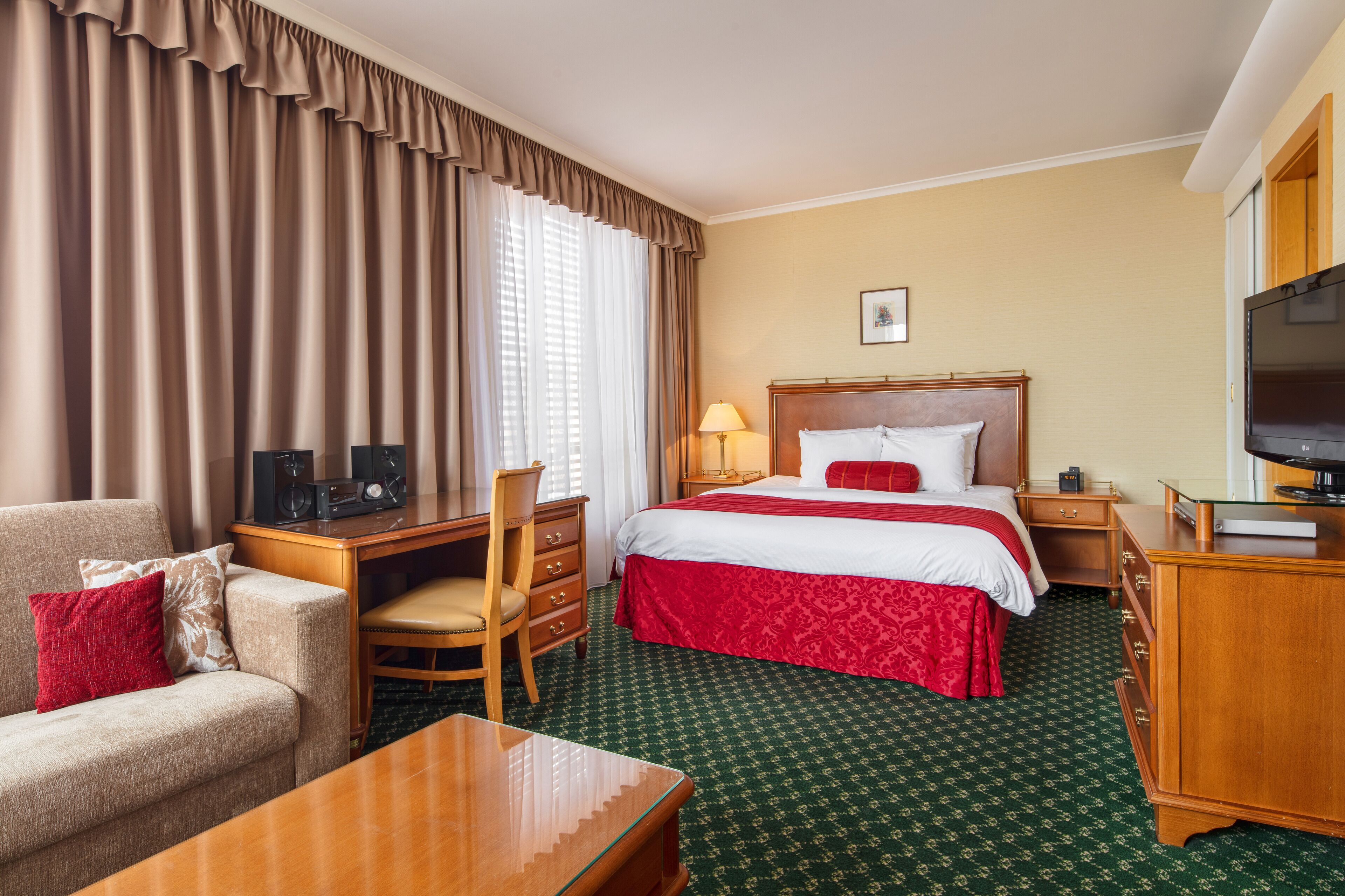 A hotel room with a bed, a desk, a chair, a television, and a window with curtains.