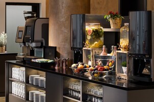 Een buffetopstelling met een koffieapparaat, schalen met fruit en een grote pot ingelegde groenten.
