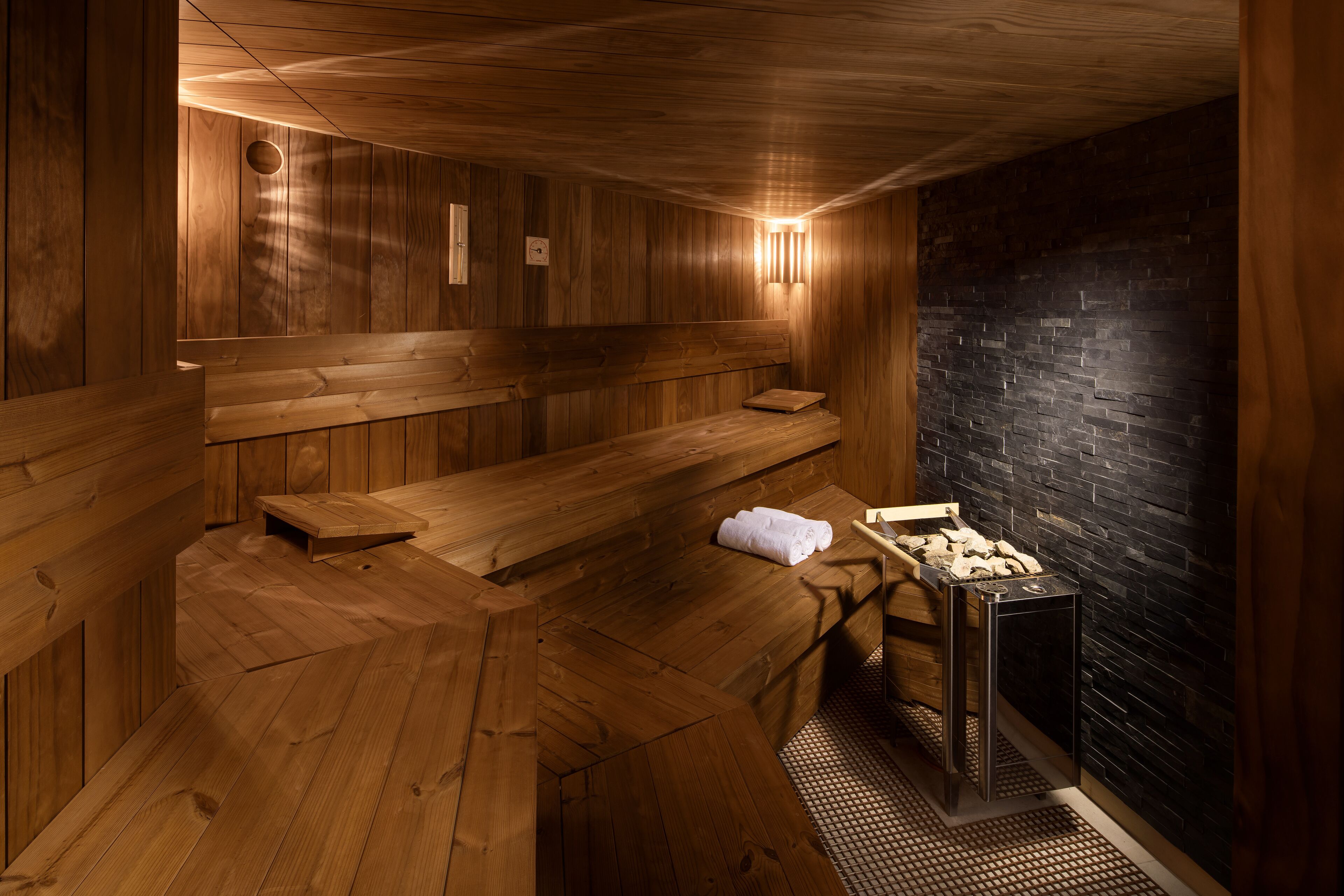 A sauna room with wooden benches, a bench with a towel, and a stone wall.