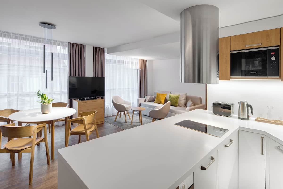 Een moderne keuken met een magnetron, broodrooster en waterkoker, een eethoek met een ronde tafel en stoelen, en een zithoek met een bank en televisie.