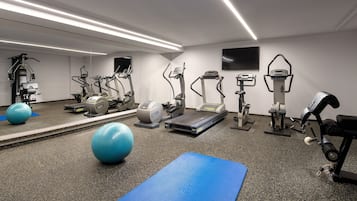A gym with exercise equipment, a blue mat, and a large mirror.